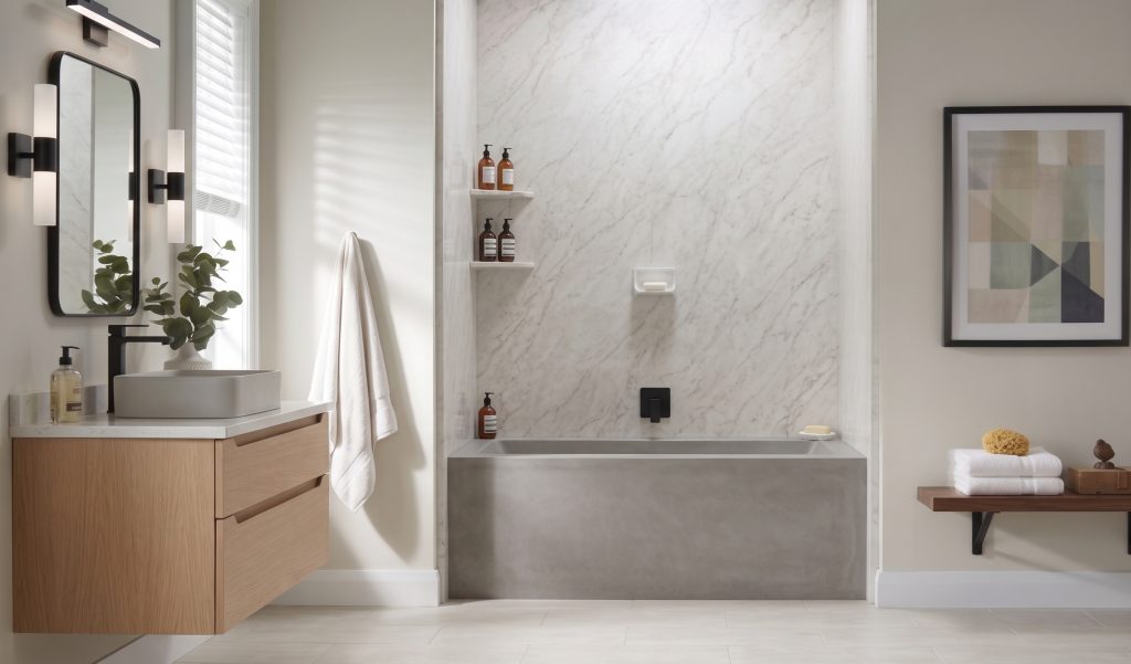 Contemporary bathroom setup showcasing a light wood floating vanity with black fixtures on the left and a minimalist gray bathtub recessed into a white marble alcove with built-in shelving.